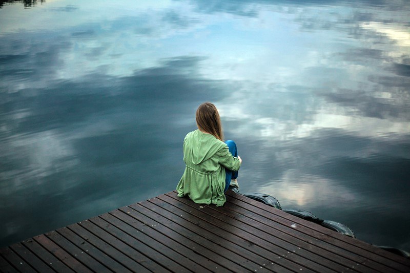 Frau sitzt allein auf Steg am Wasser