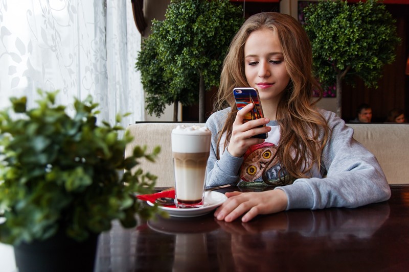 Eine junge Frau nutzt ihr Smartphone im Café